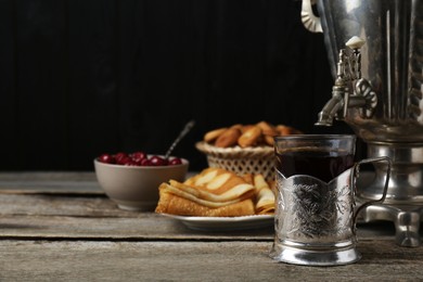 Photo of Metal samovar with cup of tea and crepes on wooden table, space for text