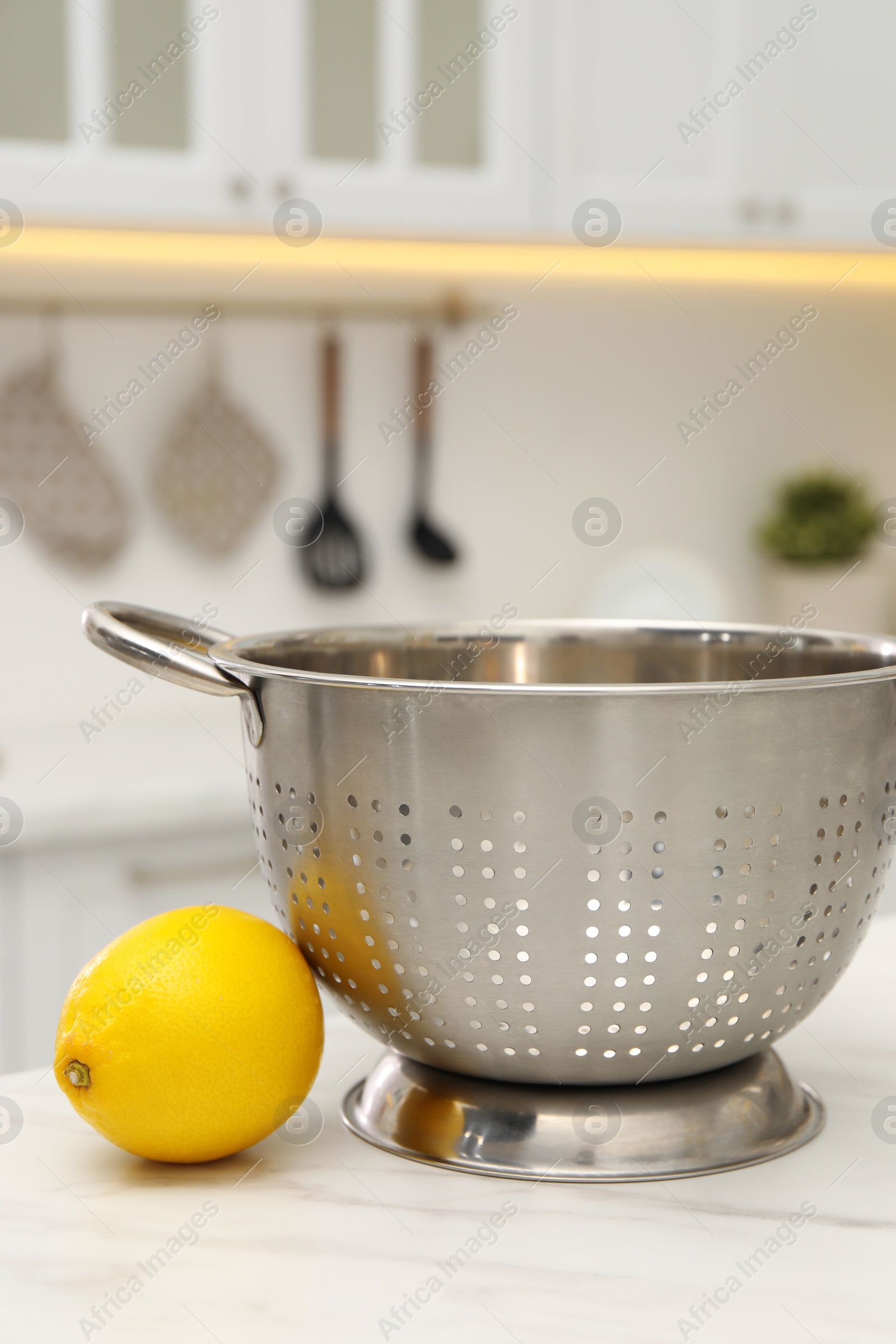 Photo of Empty colander and fresh lemon on white marble table in kitchen