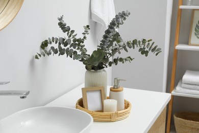 Vase with eucalyptus branches and toiletries near vessel sink in bathroom. Interior design