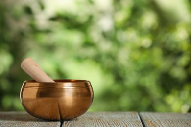 Golden singing bowl with mallet on wooden table outdoors, space for text