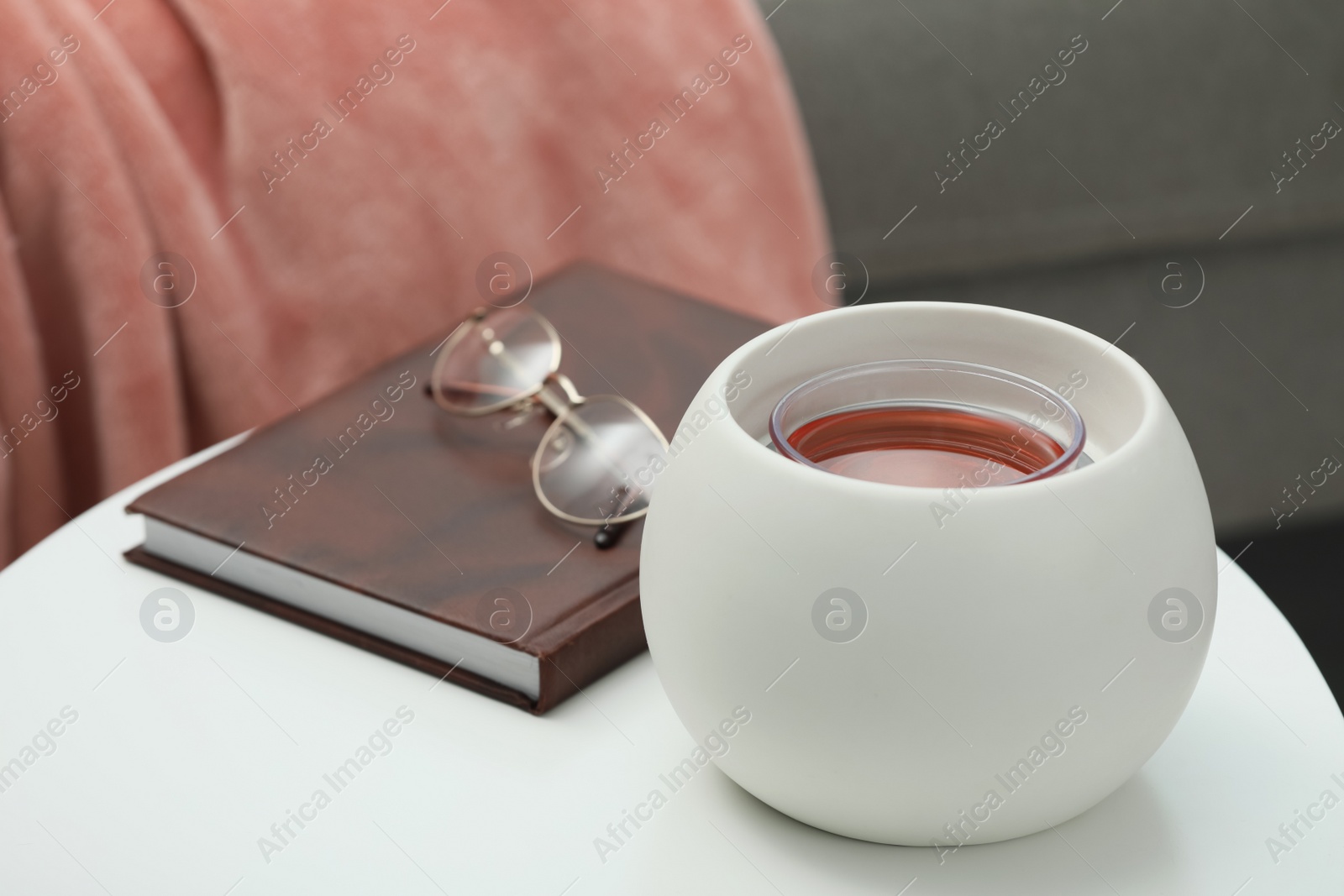 Photo of Wax air freshener, book and glasses on white table indoors. Interior element