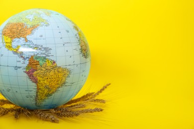 Photo of Globe with wheat spikelets on yellow background, space for text. Hunger crisis concept