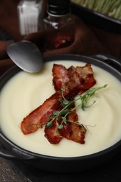 Photo of Delicious potato soup with bacon and microgreens in bowl served on wooden table, closeup