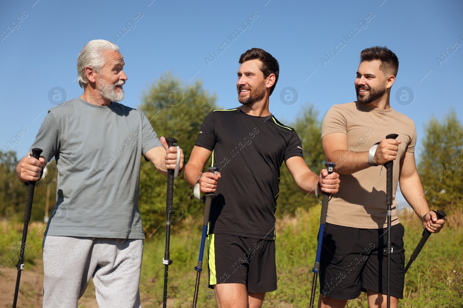 Photo of Happy men practicing Nordic walking with poles outdoors on sunny day