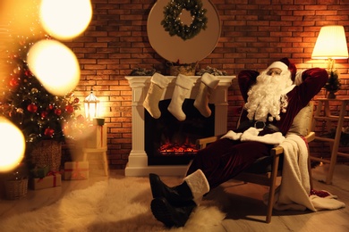 Photo of Santa Claus resting in armchair near fireplace indoors