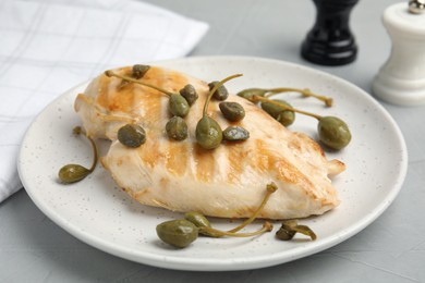 Photo of Delicious cooked chicken fillet with capers served on light grey table, closeup