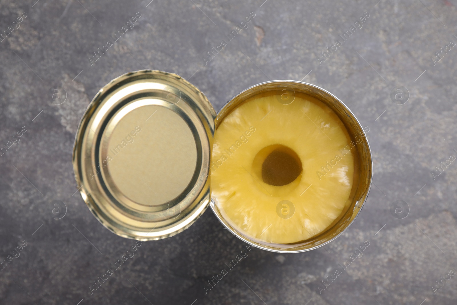 Photo of Tin with canned pineapple on grey table, top view