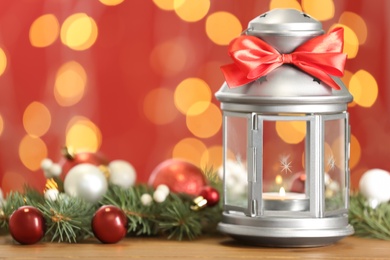 Photo of Christmas lantern with burning candle and festive ornaments on wooden table against blurred lights. Space for text