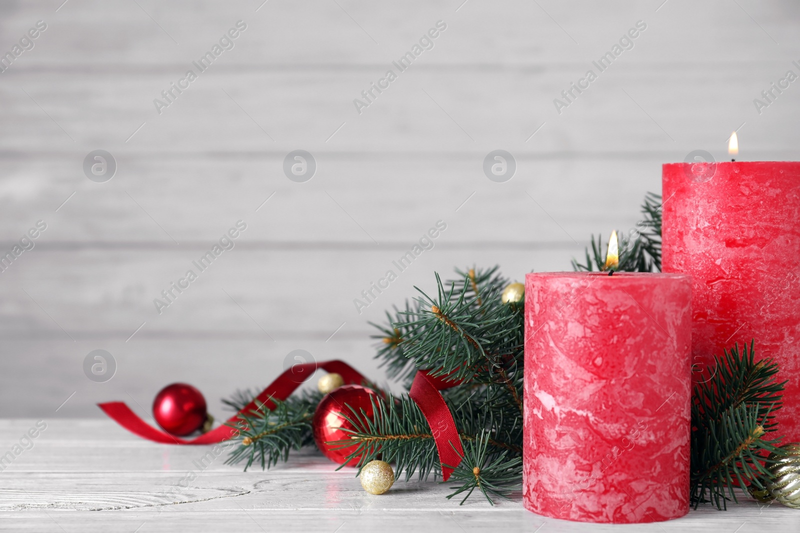 Photo of Burning red candles with Christmas decor on wooden table against light background. Space for text