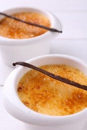 Photo of Delicious creme brulee in bowls and vanilla pods on white table, closeup