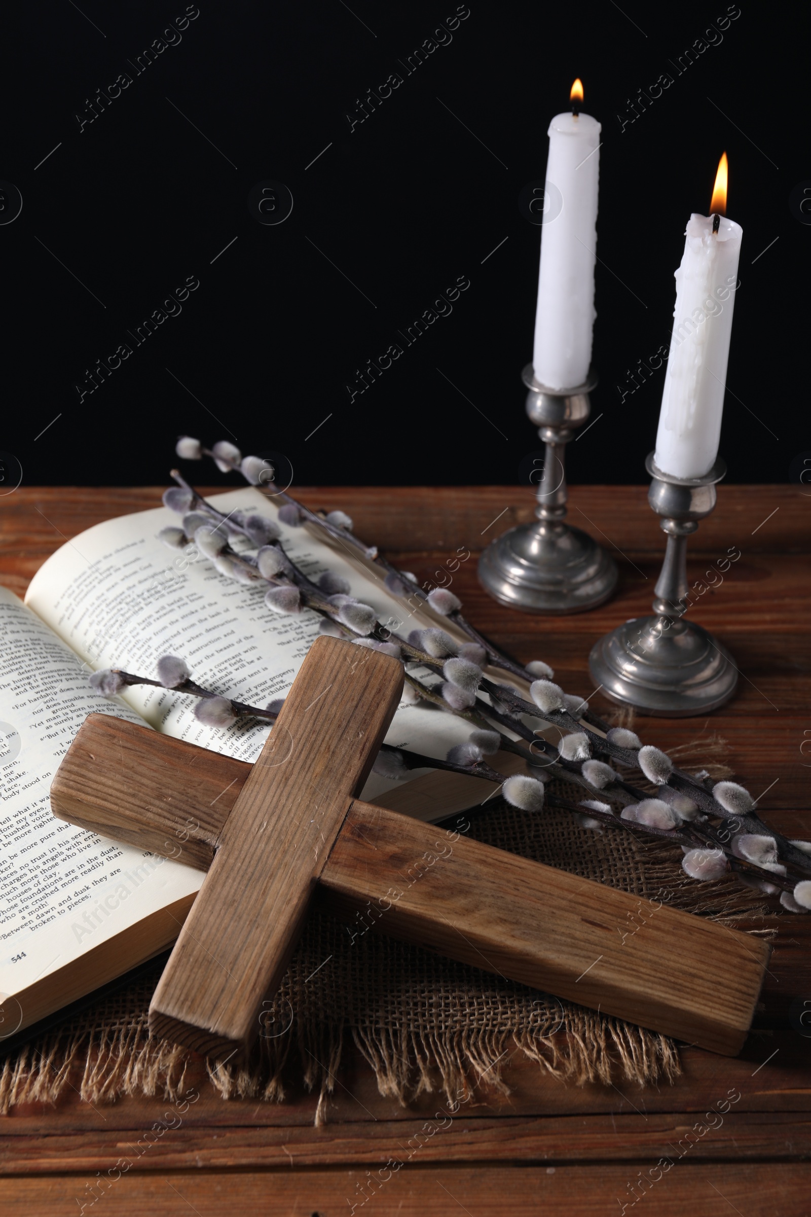 Photo of Burning church candles, cross, Bible and willow branches on wooden table