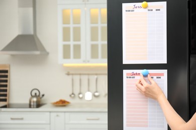 Photo of Woman putting blank to do list on refrigerator door in kitchen, closeup. Space for text