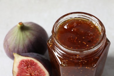 Jar of tasty sweet jam and fresh figs on table, closeup