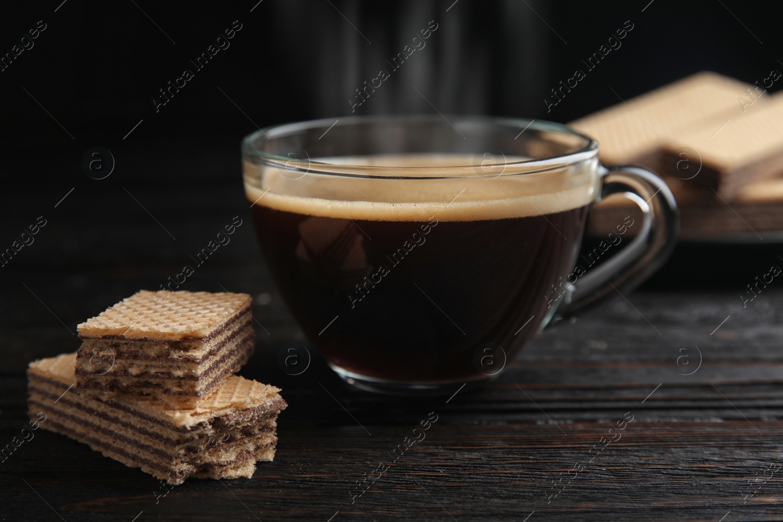 Photo of Delicious wafers and coffee on black wooden table