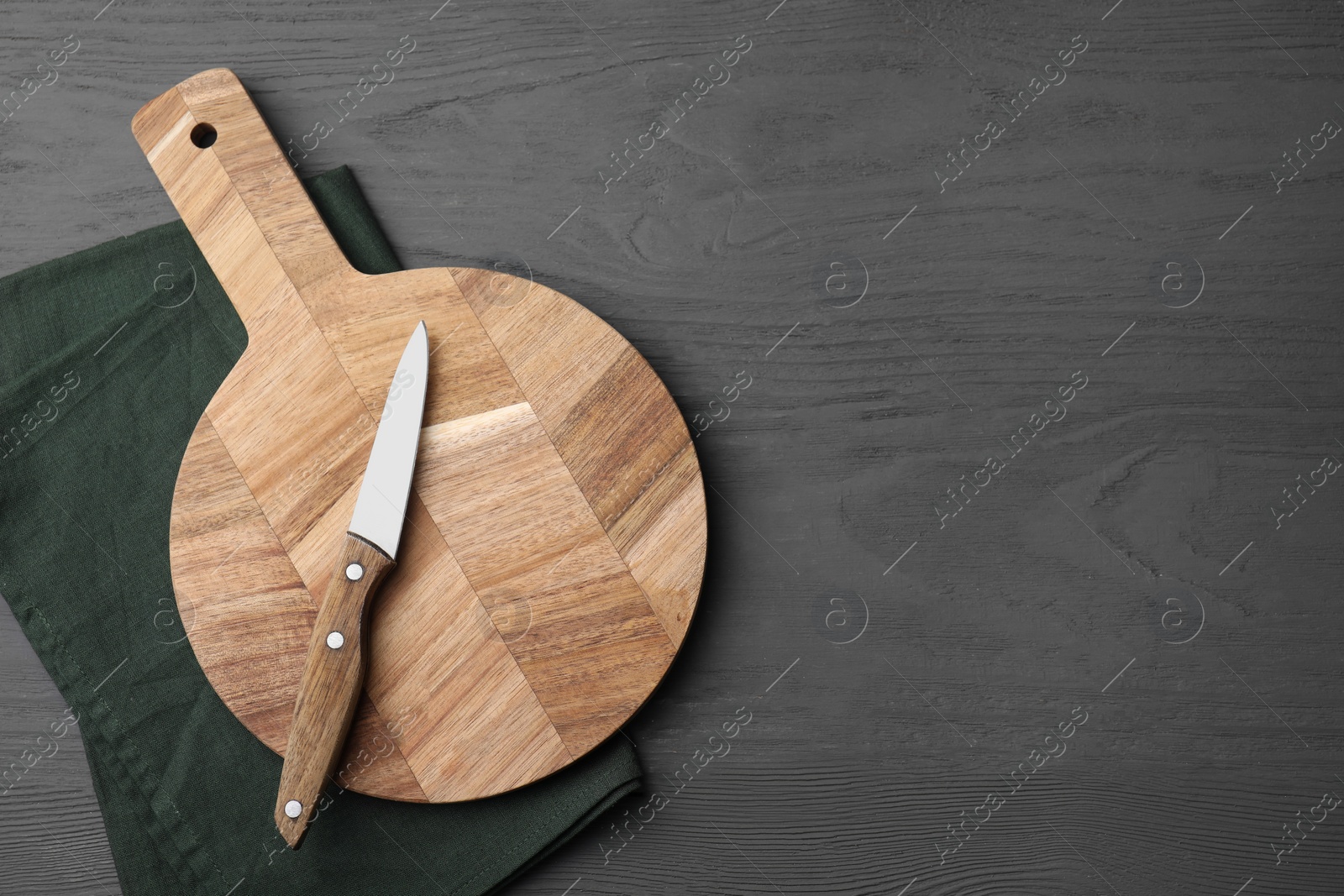 Photo of Wooden board, knife and napkin on grey table, top view. Space for text