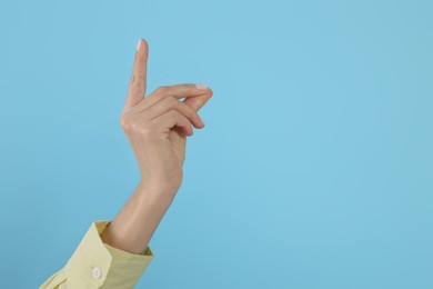 Woman snapping fingers on light blue background, closeup of hand. Space for text