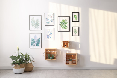 Beautiful paintings of tropical leaves on white wall in living room interior