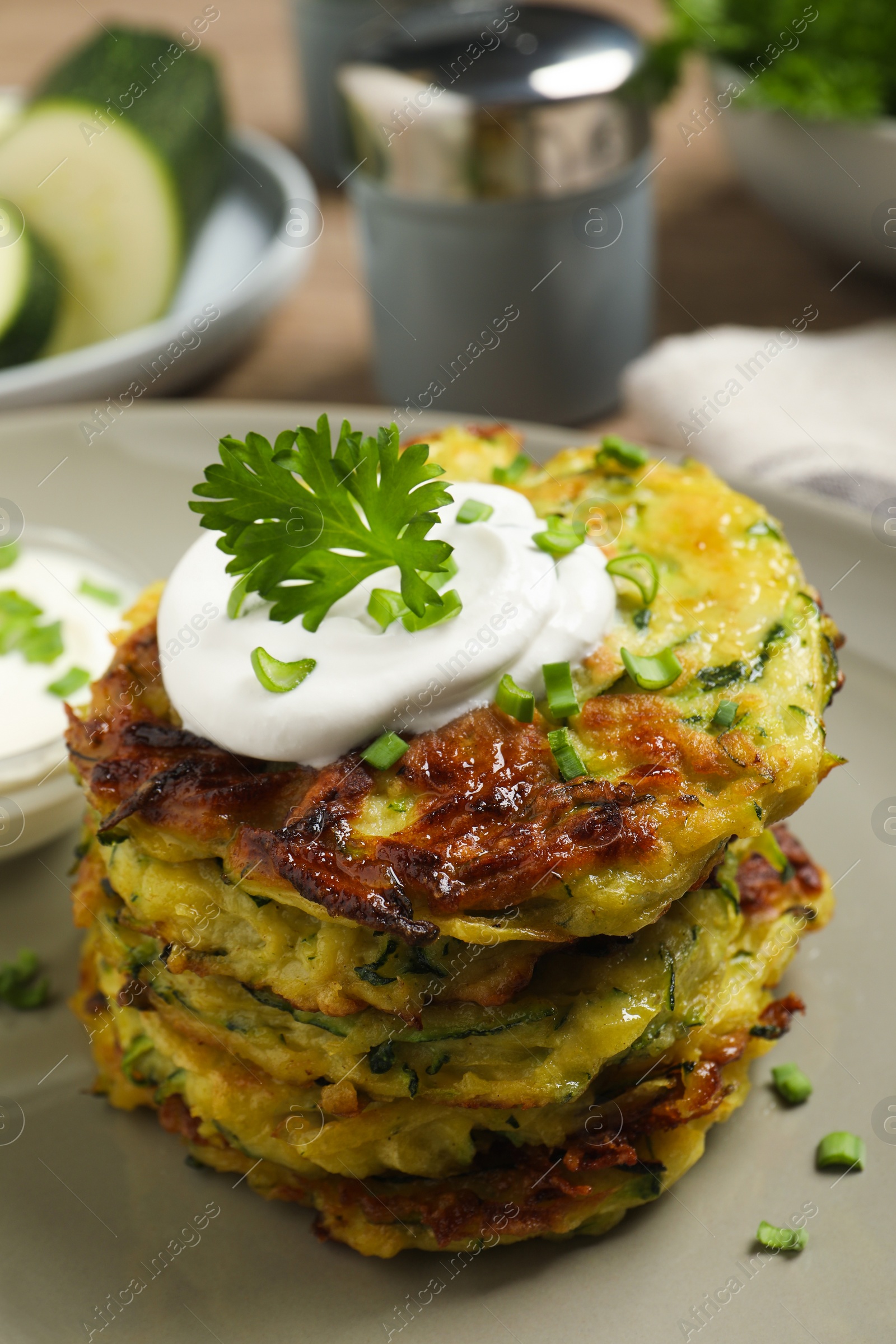 Photo of Delicious zucchini fritters with sour cream on plate, closeup