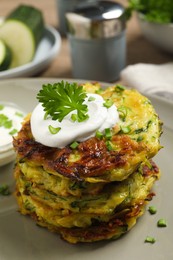 Photo of Delicious zucchini fritters with sour cream on plate, closeup
