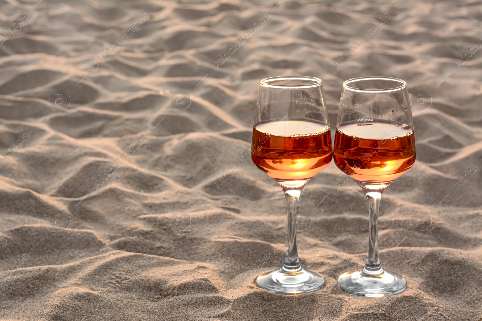 Photo of Glasses of tasty rose wine on sand, space for text