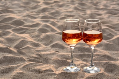 Photo of Glassestasty rose wine on sand, space for text