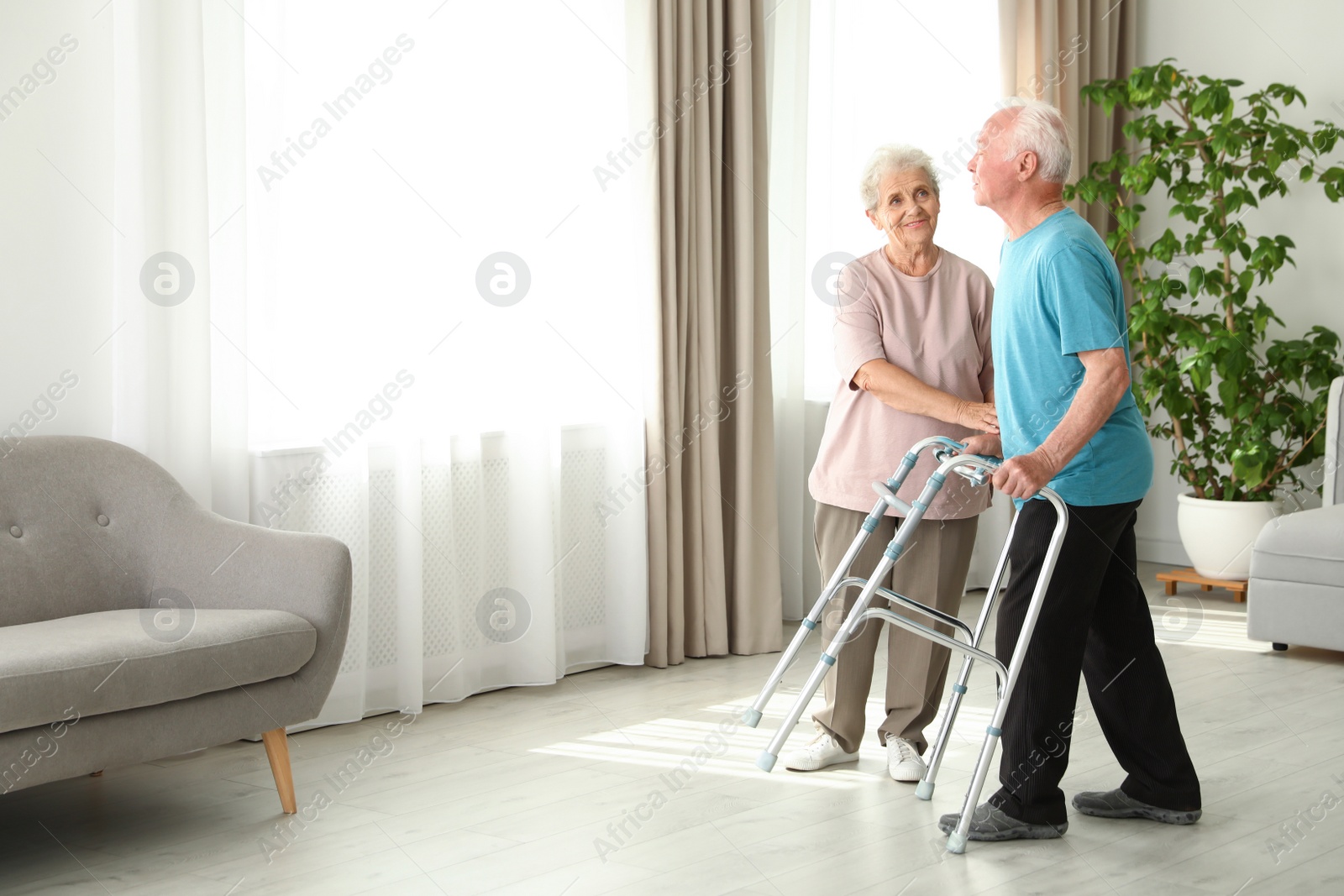 Photo of Elderly woman and her husband with walking frame indoors. Space for text