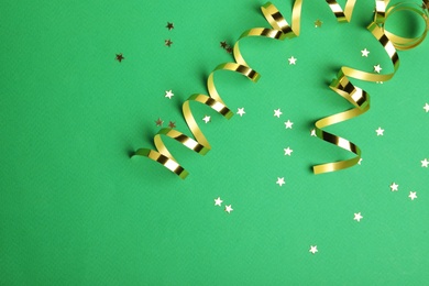 Photo of Shiny golden serpentine streamers and confetti on green background, flat lay. Space for text