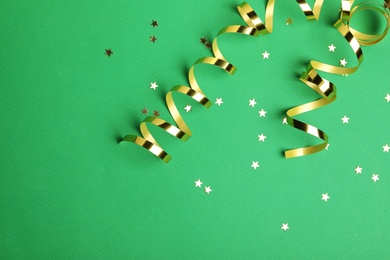 Shiny golden serpentine streamers and confetti on green background, flat lay. Space for text