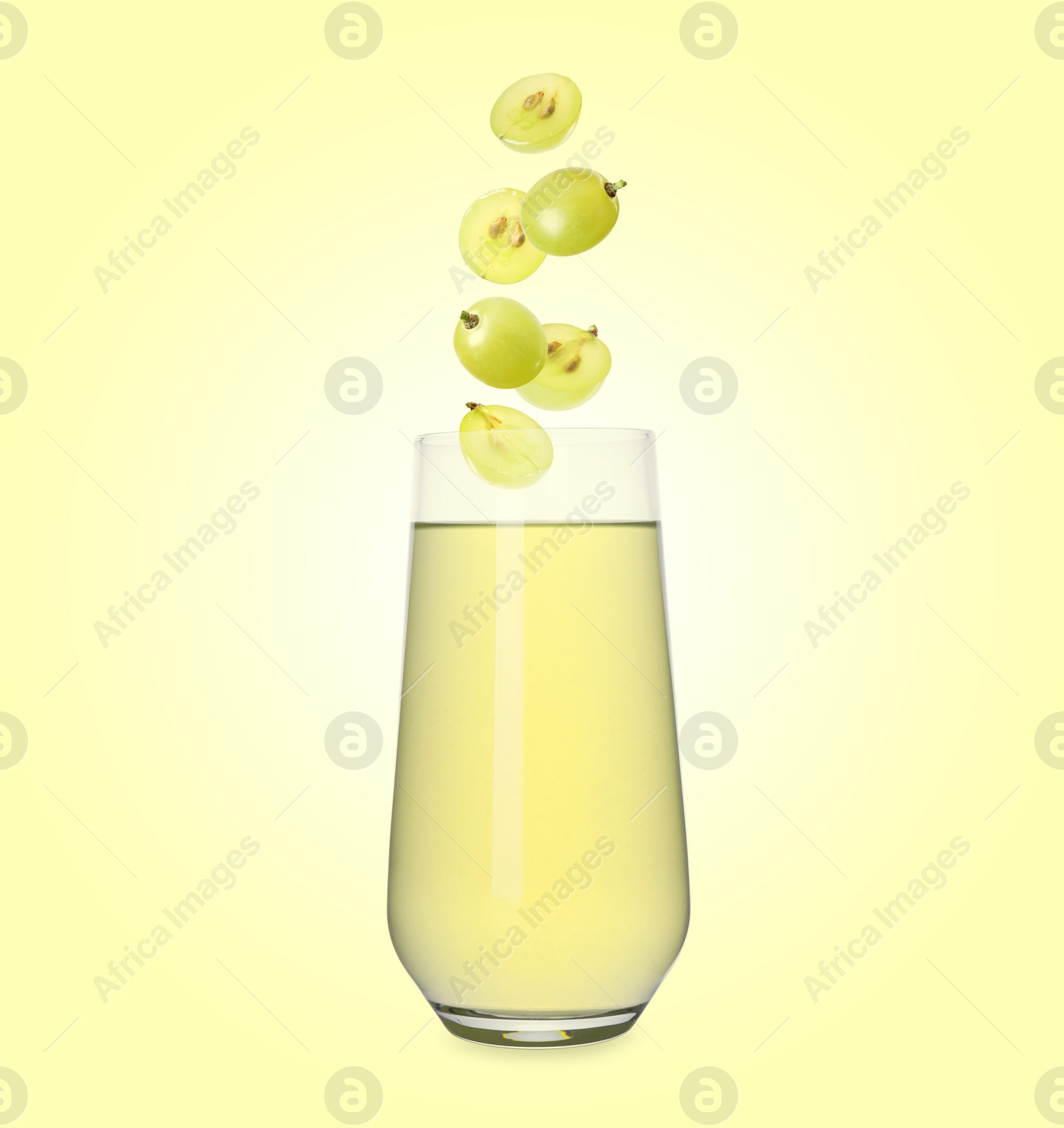 Image of Freshly made grape juice on pale yellow background. Cut and whole berries falling into glass