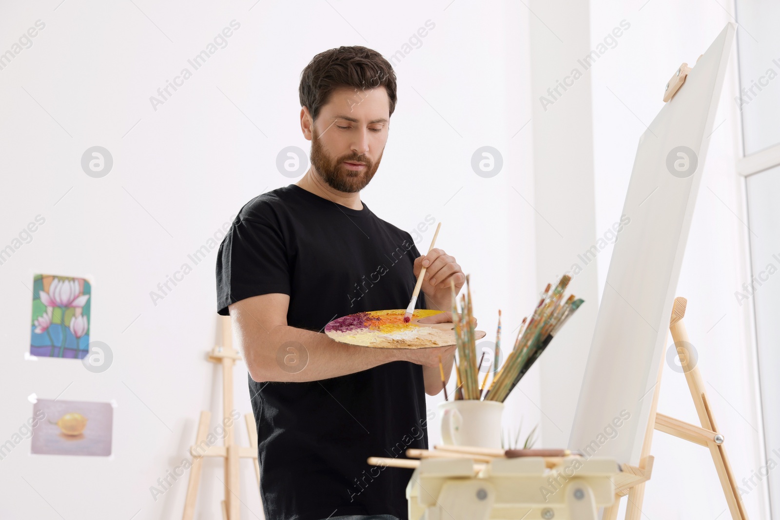 Photo of Man painting in studio. Using easel to hold canvas