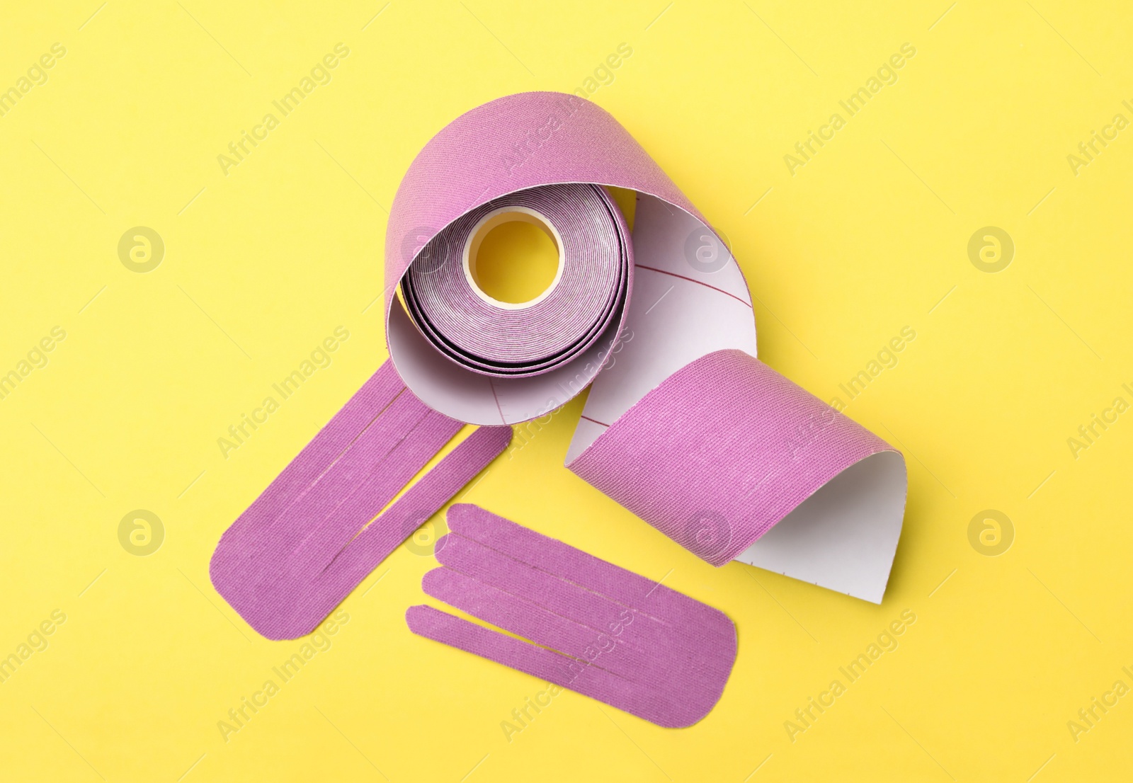 Photo of Bright kinesio tape roll and pieces on yellow background, flat lay