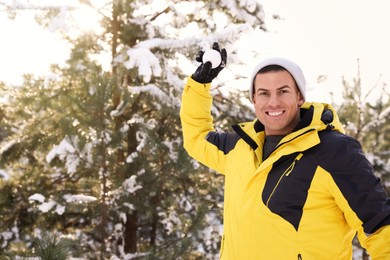 Happy man throwing snowball outdoors on winter day