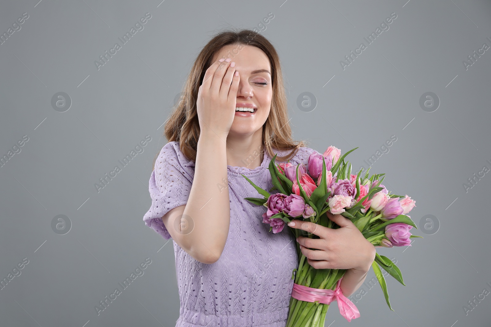 Photo of Happy young woman with bouquet of beautiful tulips on grey background