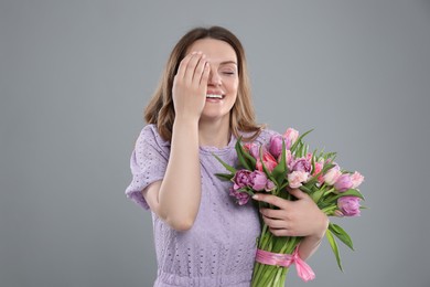 Happy young woman with bouquet of beautiful tulips on grey background