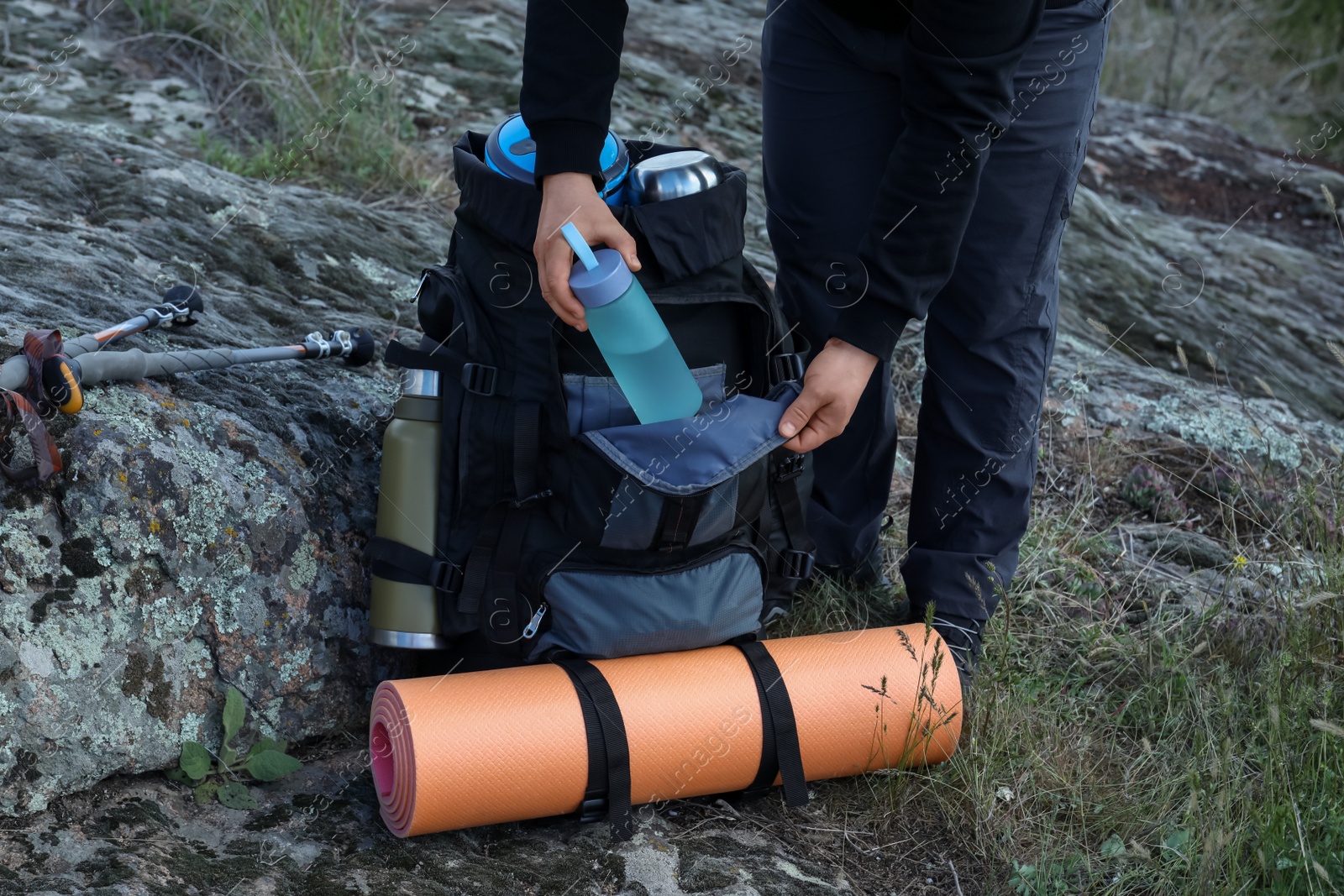 Photo of Hiker putting bottle of water into backpack on rocky hill, closeup