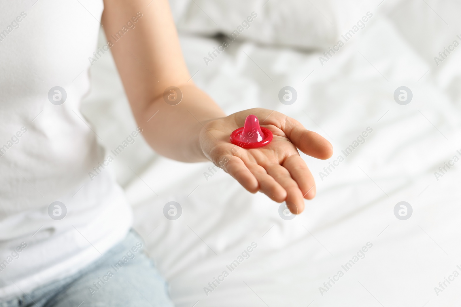 Photo of Woman holding unpacked condom on bed, closeup. Safe sex