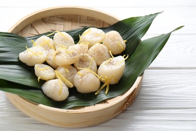 Photo of Raw scallops with milled pepper and lemon zest on white wooden table, closeup