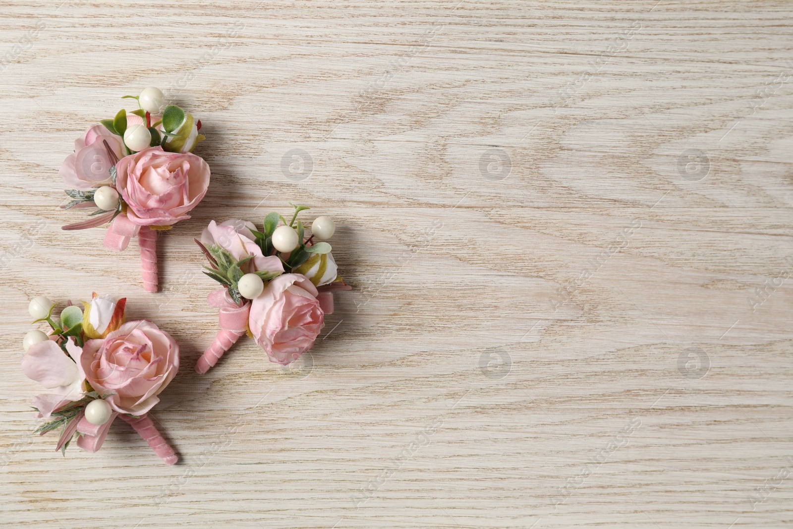 Photo of Stylish pink boutonnieres on white wooden table, flat lay. Space for text