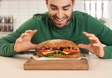 Young hungry man and tasty sandwich in kitchen