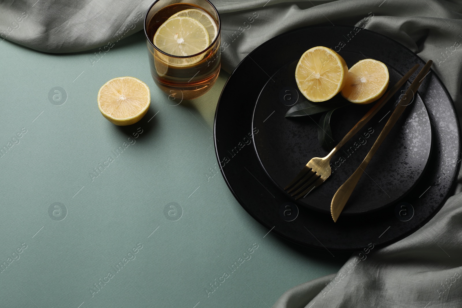 Photo of Stylish table setting. Plates, cutlery and tea with lemon on olive background, above view. Space for text