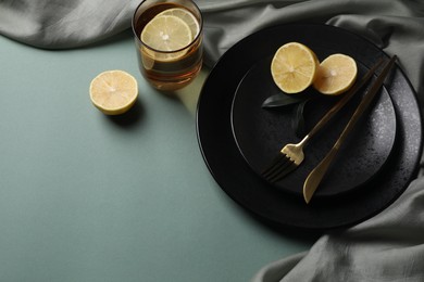 Stylish table setting. Plates, cutlery and tea with lemon on olive background, above view. Space for text