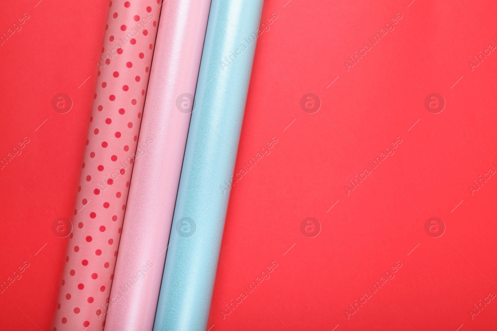 Photo of Rolls of colorful wrapping papers on red background, flat lay. Space for text