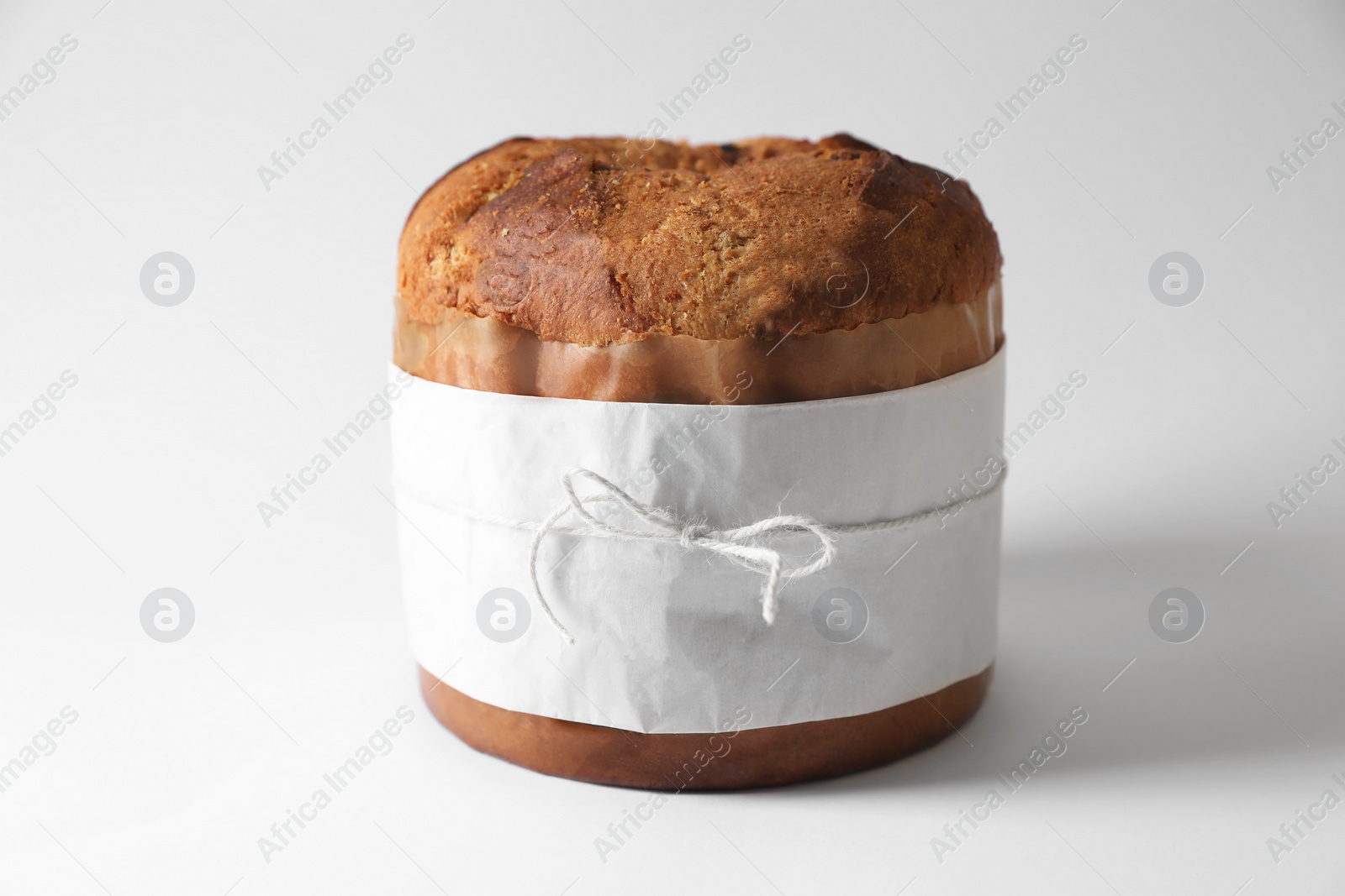 Photo of Delicious Panettone cake wrapped in parchment paper on white background. Traditional Italian pastry