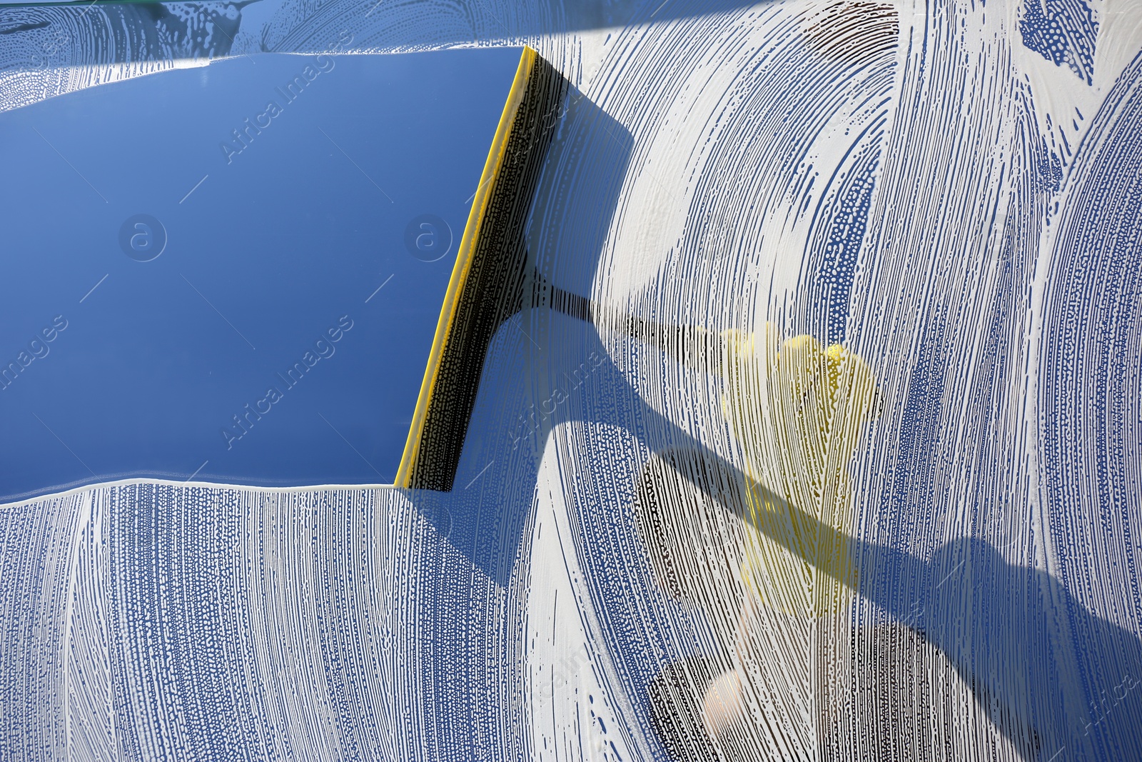 Photo of Woman cleaning glass with squeegee on sunny day, closeup