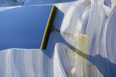 Woman cleaning glass with squeegee on sunny day, closeup