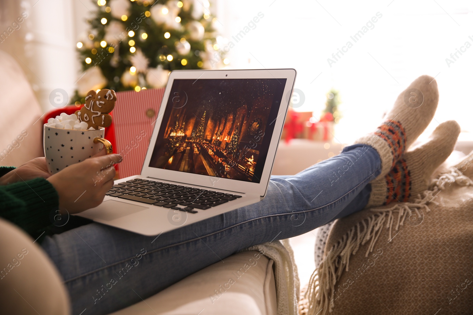 Photo of MYKOLAIV, UKRAINE - DECEMBER 25, 2020: Woman with sweet drink watching Harry Potter and Philosopher's stone movie on laptop at home, closeup. Cozy winter holidays atmosphere