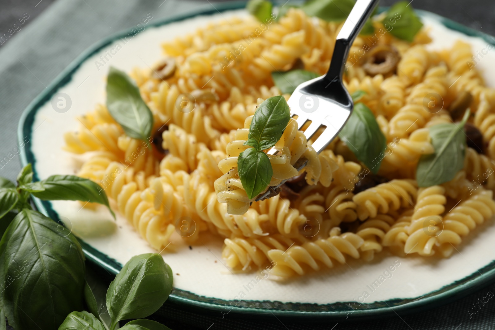 Photo of Delicious pasta with basil on fork over plate, closeup