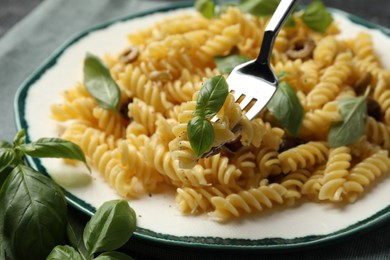 Delicious pasta with basil on fork over plate, closeup