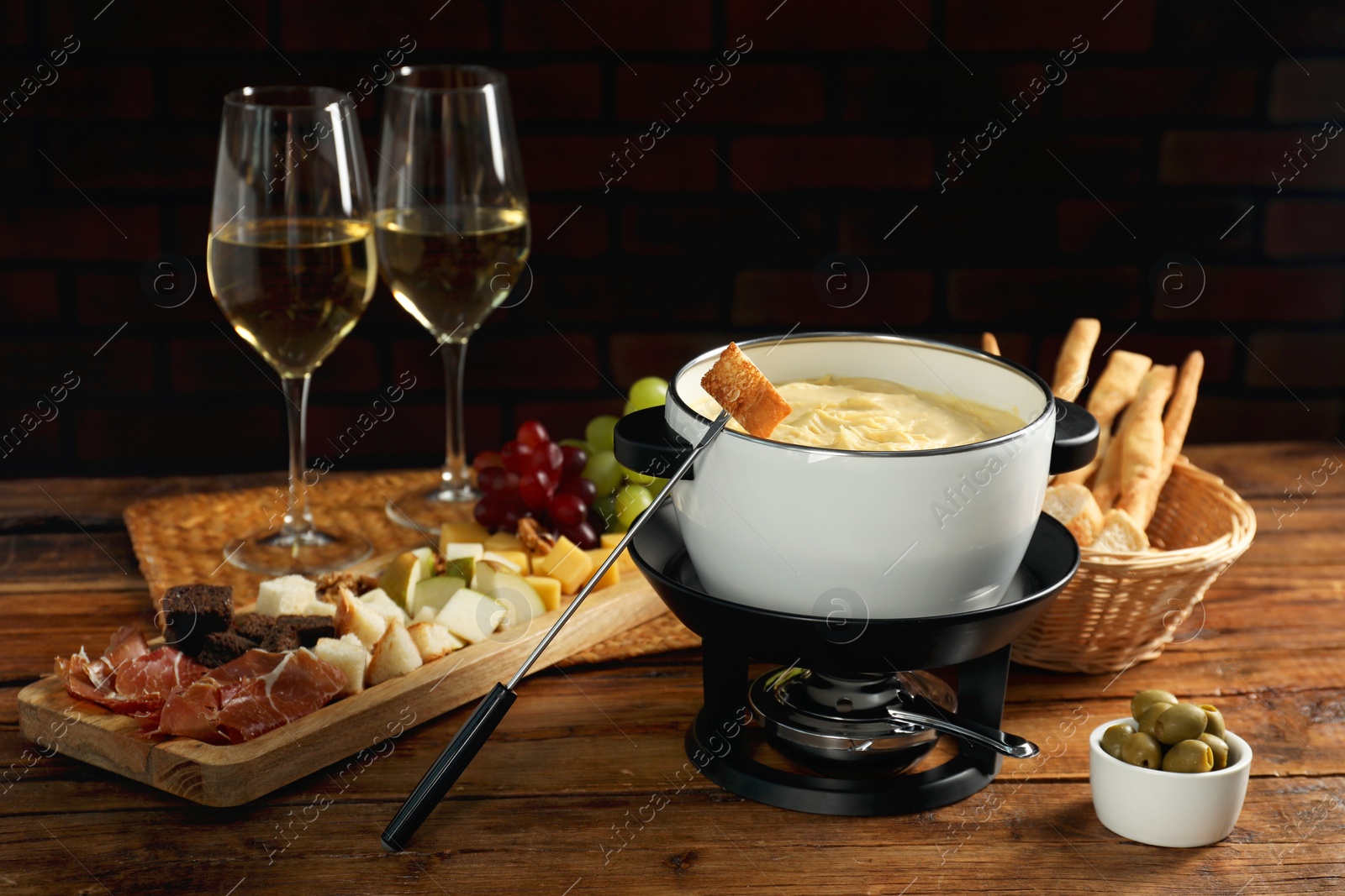 Photo of Fondue with tasty melted cheese, forks, different snacks and wine on wooden table