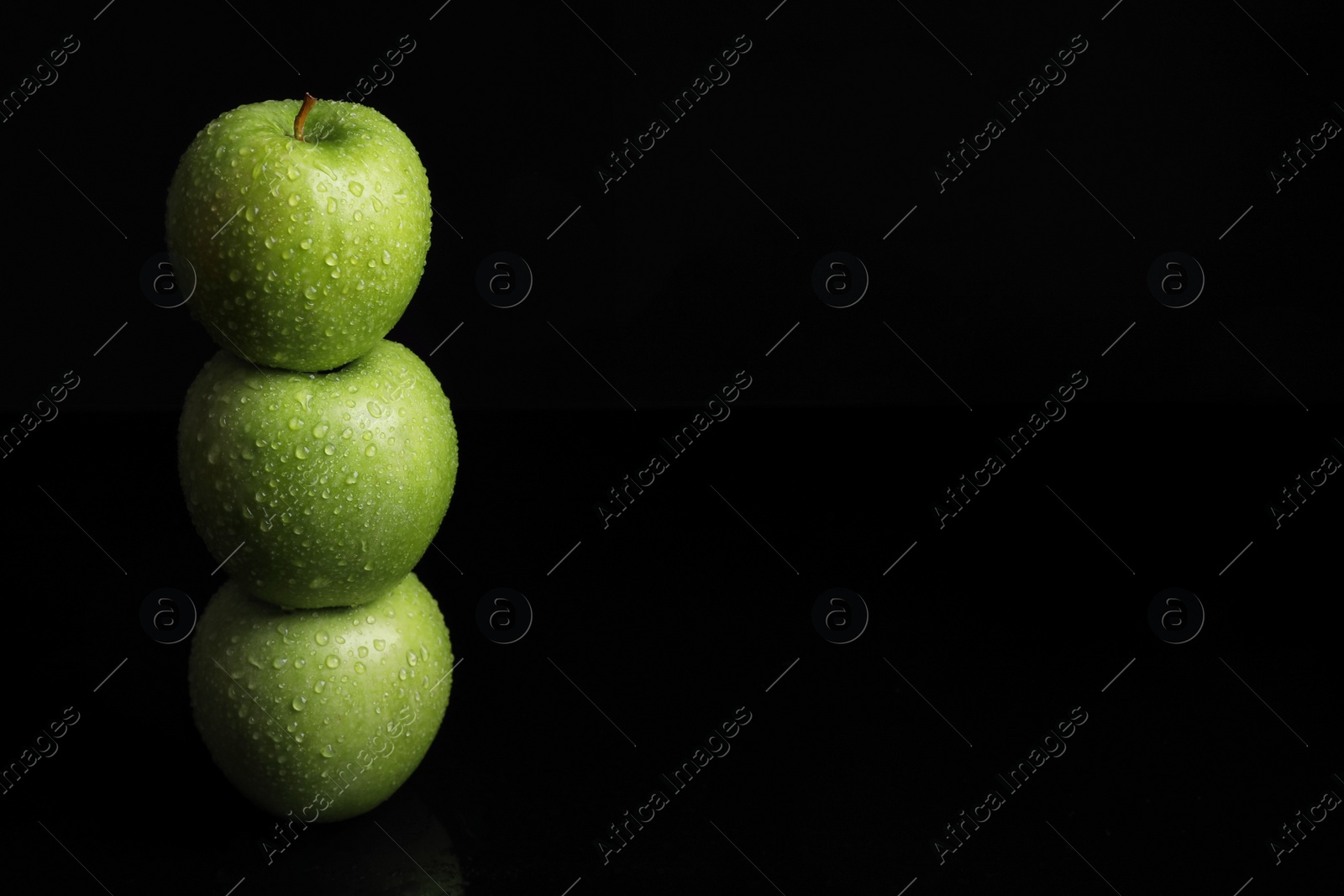 Photo of Stack of green apples with water drops on black background. Space for text